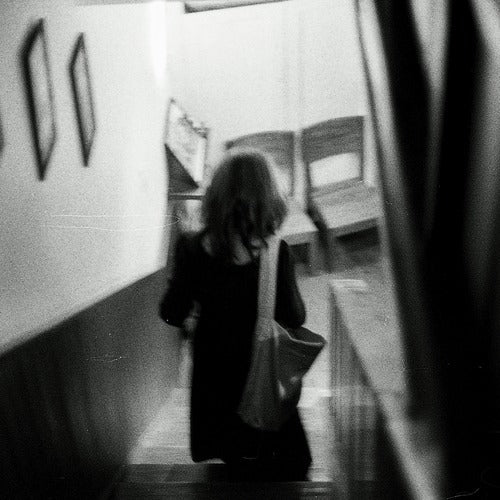 Grainy black-and-white image of a woman descending a staircase with soft motion blur, evoking a candid and introspective mood perfect for storytelling or artistic photography themes.