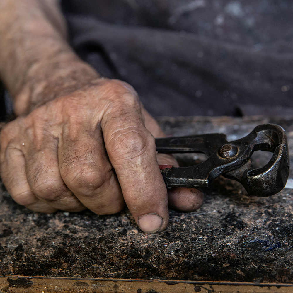 Close-up of a weathered hand holding a vintage metal tool against a gritty work surface, embodying craftsmanship, resilience, and tradition.