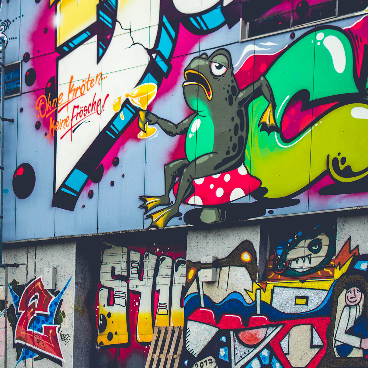 Vivid urban street art featuring a whimsical frog holding a champagne glass while sitting on a mushroom, surrounded by bold graffiti and dynamic colors, embodying creativity and rebellion.