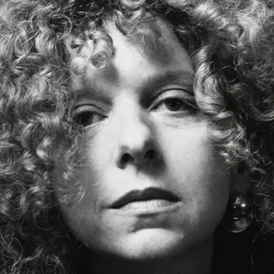 Black-and-white close-up portrait of a woman with curly hair and large earrings, gazing directly at the camera with a serious expression.