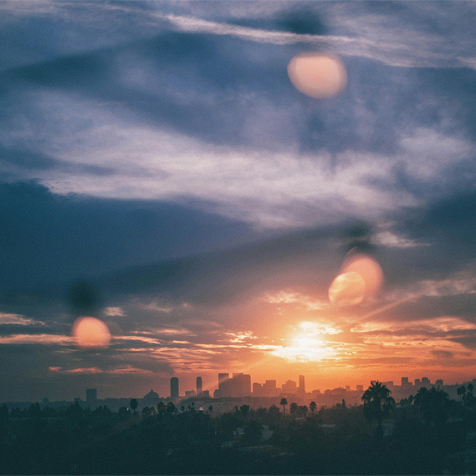 Dreamy cityscape at sunset with soft bokeh lights in the foreground, blending urban silhouettes and vibrant hues of orange and blue for a tranquil, cinematic feel.