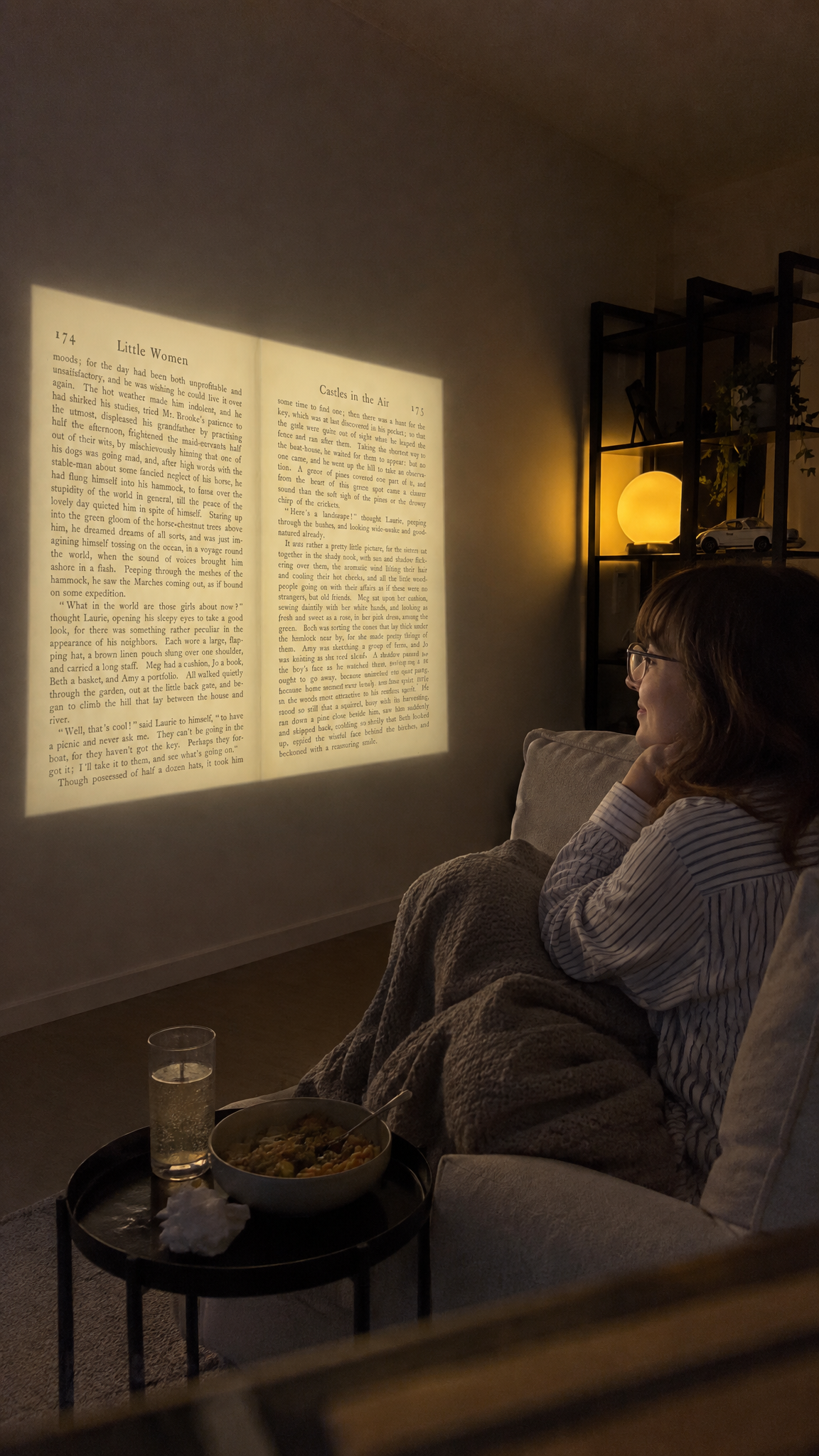 A reader curled on the sofa at night with her book projected on the bare wall in front of her