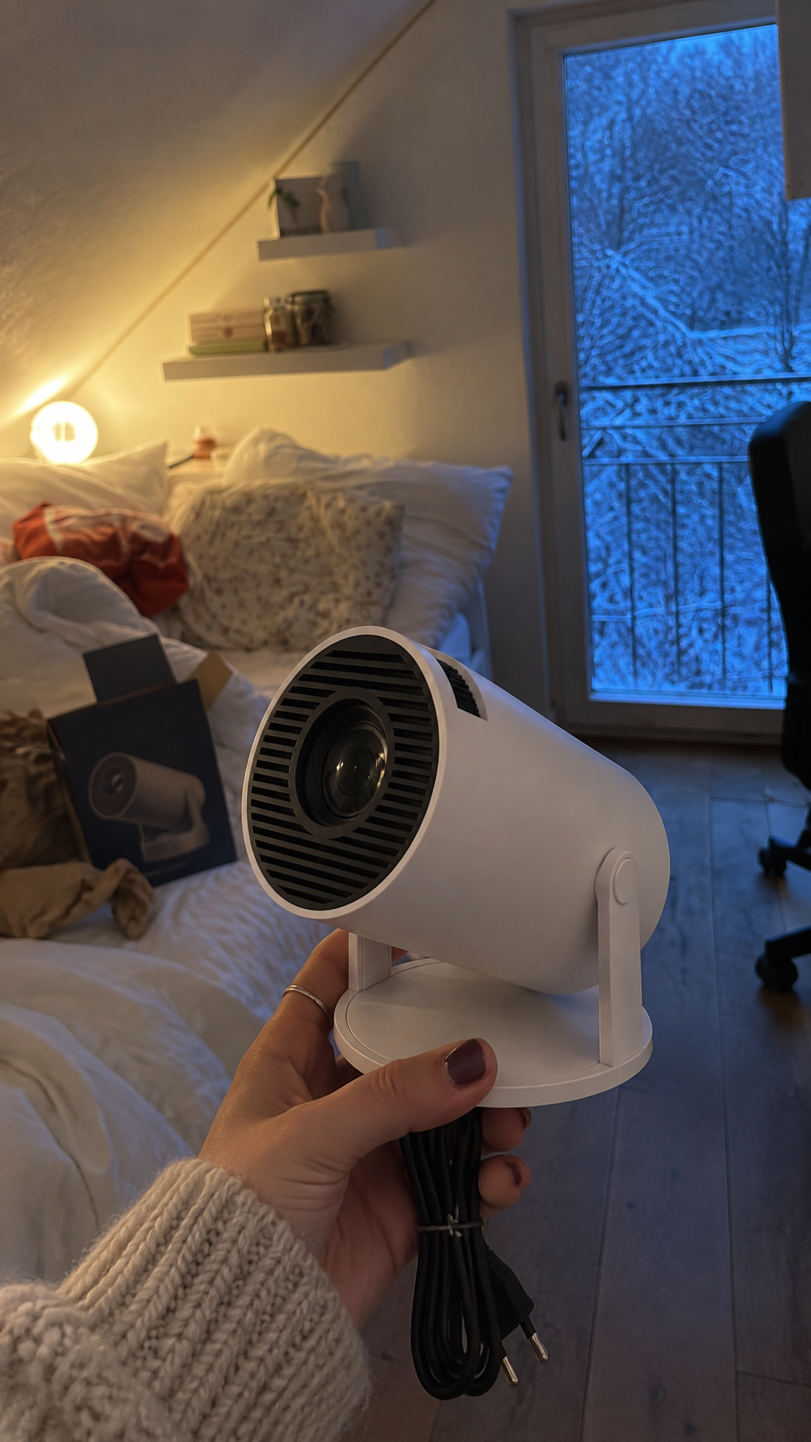 Holding the just-unboxed projector out to the camera in an attic bedroom at dusk