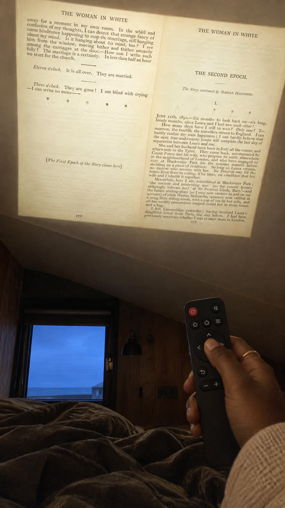 Looking up from the pillow at a page projected on the sloped attic ceiling, remote in hand
